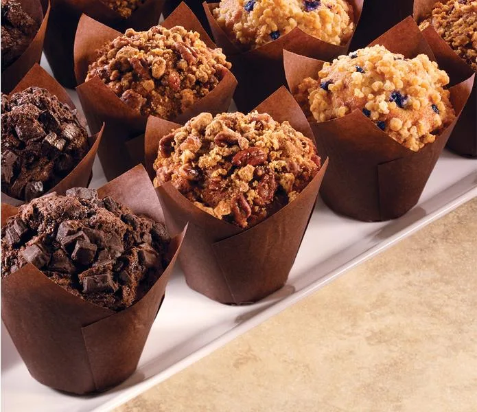 Variety of fresh-baked muffins in brown paper liners, including chocolate and berry flavors, ideal for food service wholesale distribution.
