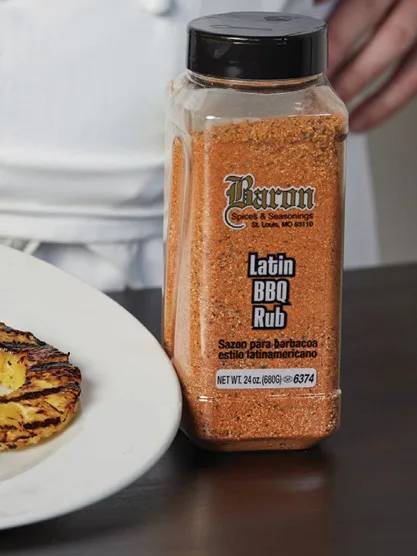 Baron Latin BBQ Rub seasoning in bulk container with grilled food, for professional foodservice and wholesale distribution.