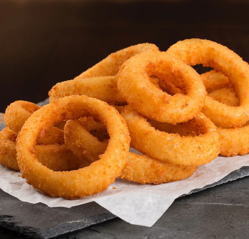Golden-brown breaded onion rings stacked on parchment paper, ideal for foodservice suppliers and commercial food distributors.