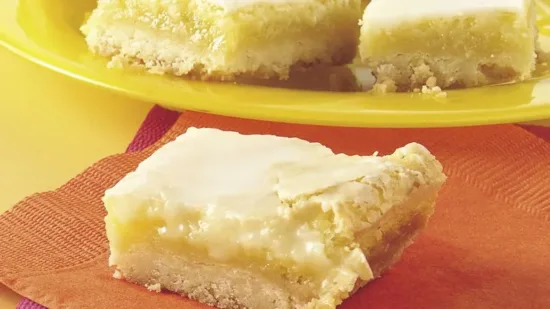 Golden lemon bars with white frosting topping displayed on yellow plate, ideal for food service wholesale distribution.