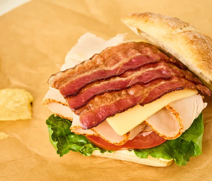 Gourmet BLT sandwich featuring crispy bacon strips, sliced turkey, cheese, tomato, and fresh lettuce on toasted bread for foodservice.
