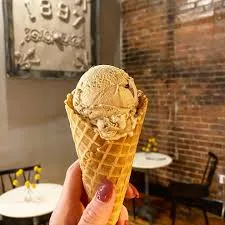 Hand holding a generous scoop of vanilla ice cream in a crispy waffle cone, perfect for food service operations and dessert distribution.